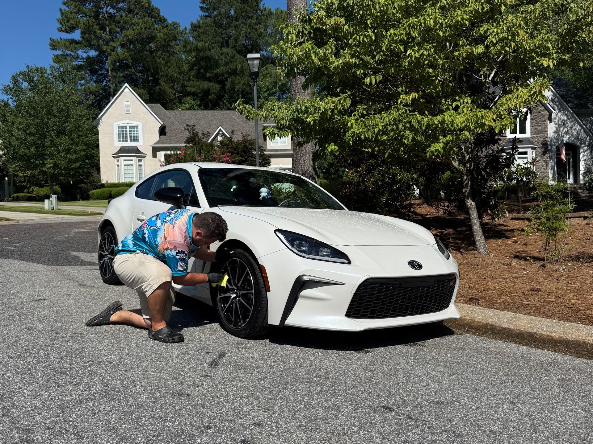 A man is kneeling down next to a white sports car on the side of the road.