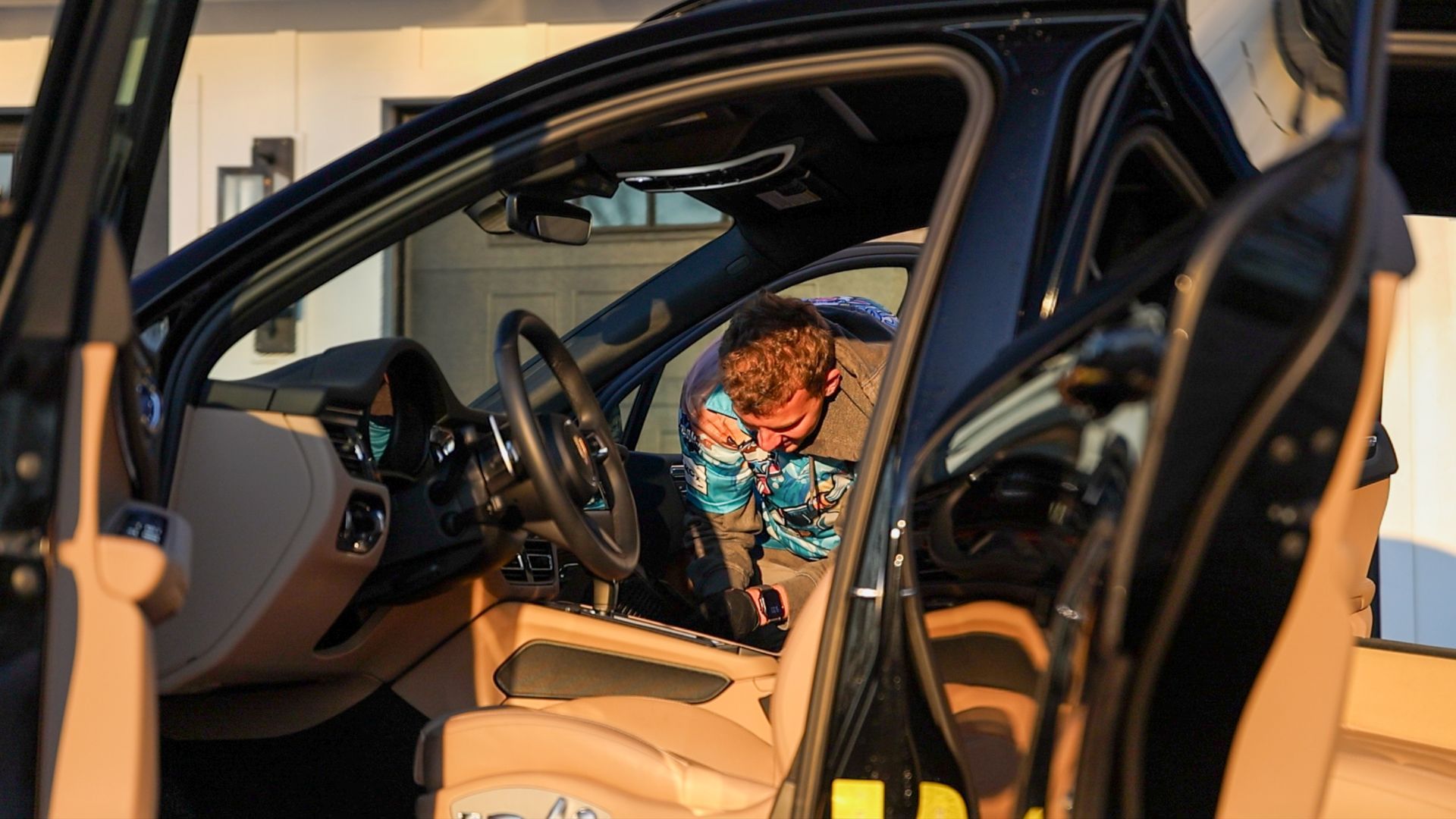 A man is sitting in the driver 's seat of a car with the door open.