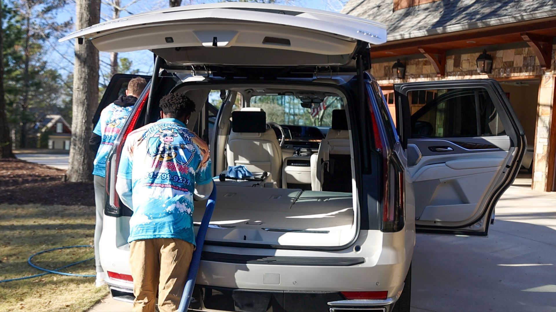 A man is cleaning the back of a car with a vacuum cleaner.