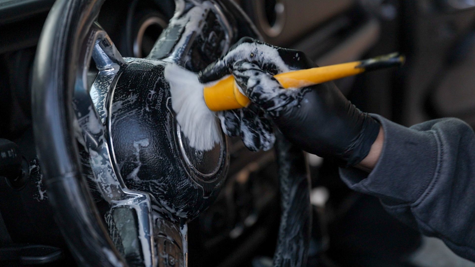 A person is cleaning the steering wheel of a car with a brush.