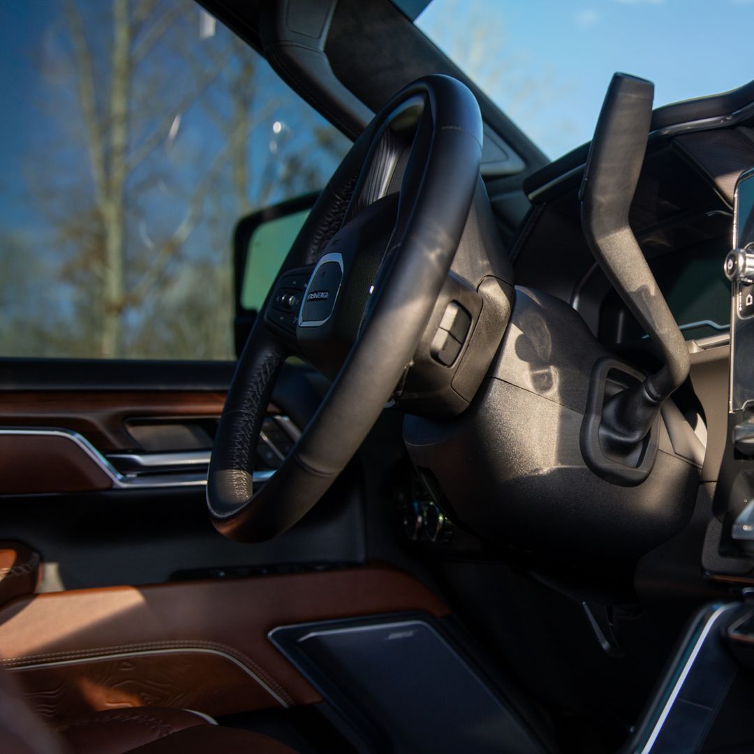 The back seat of a truck with brown leather seats and a sun shining through the window.