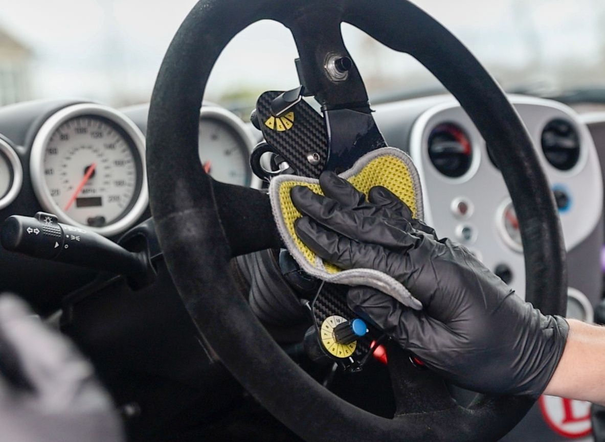 A person wearing black gloves is cleaning the steering wheel of a car.
