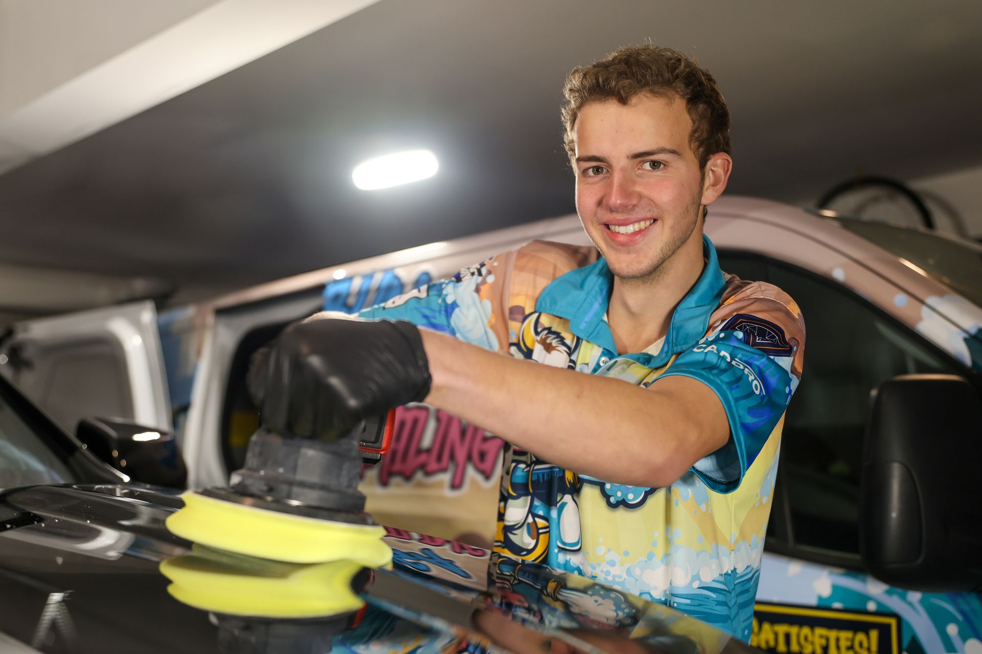 A young man is polishing a car with a machine.