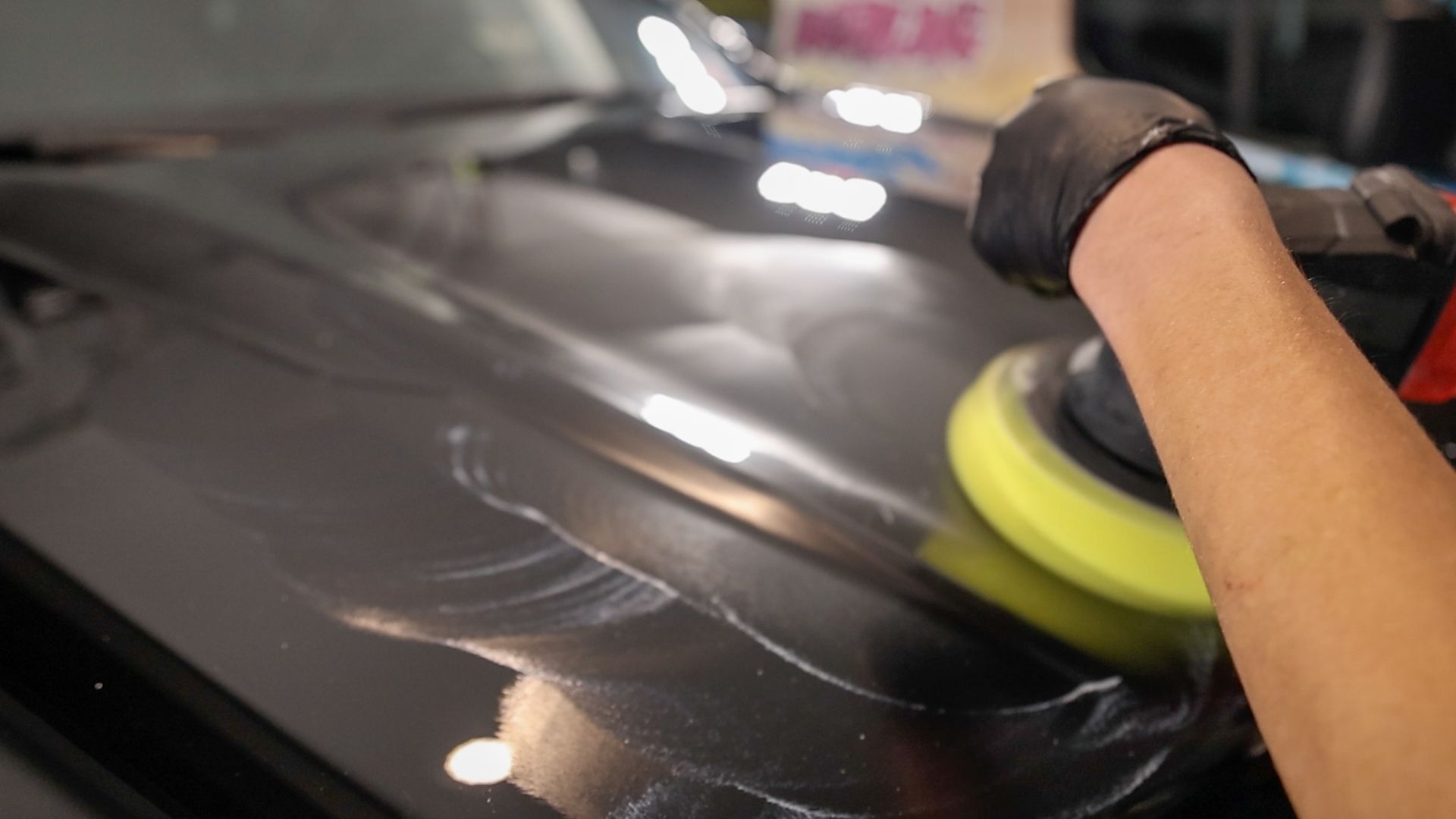 A man is polishing the hood of a car with a machine.