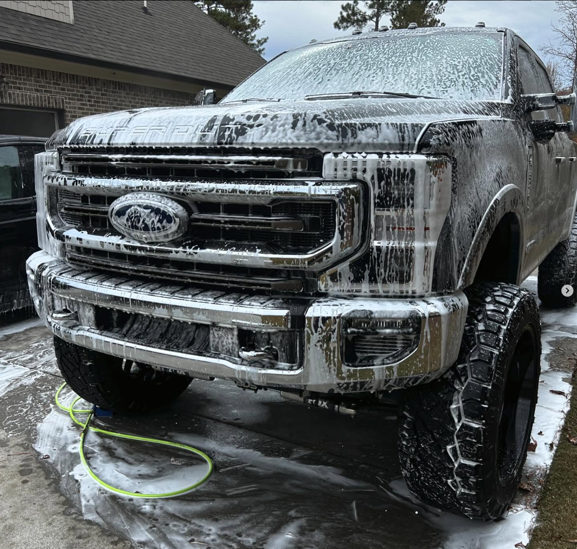 A black car is covered in foam at a car wash.