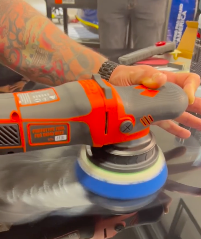 A man is polishing a red car with a polisher.