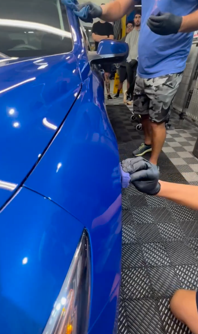 A man is cleaning a blue car in a garage.