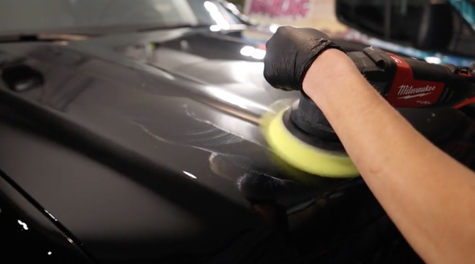 A person is polishing a black car with a yellow polisher.