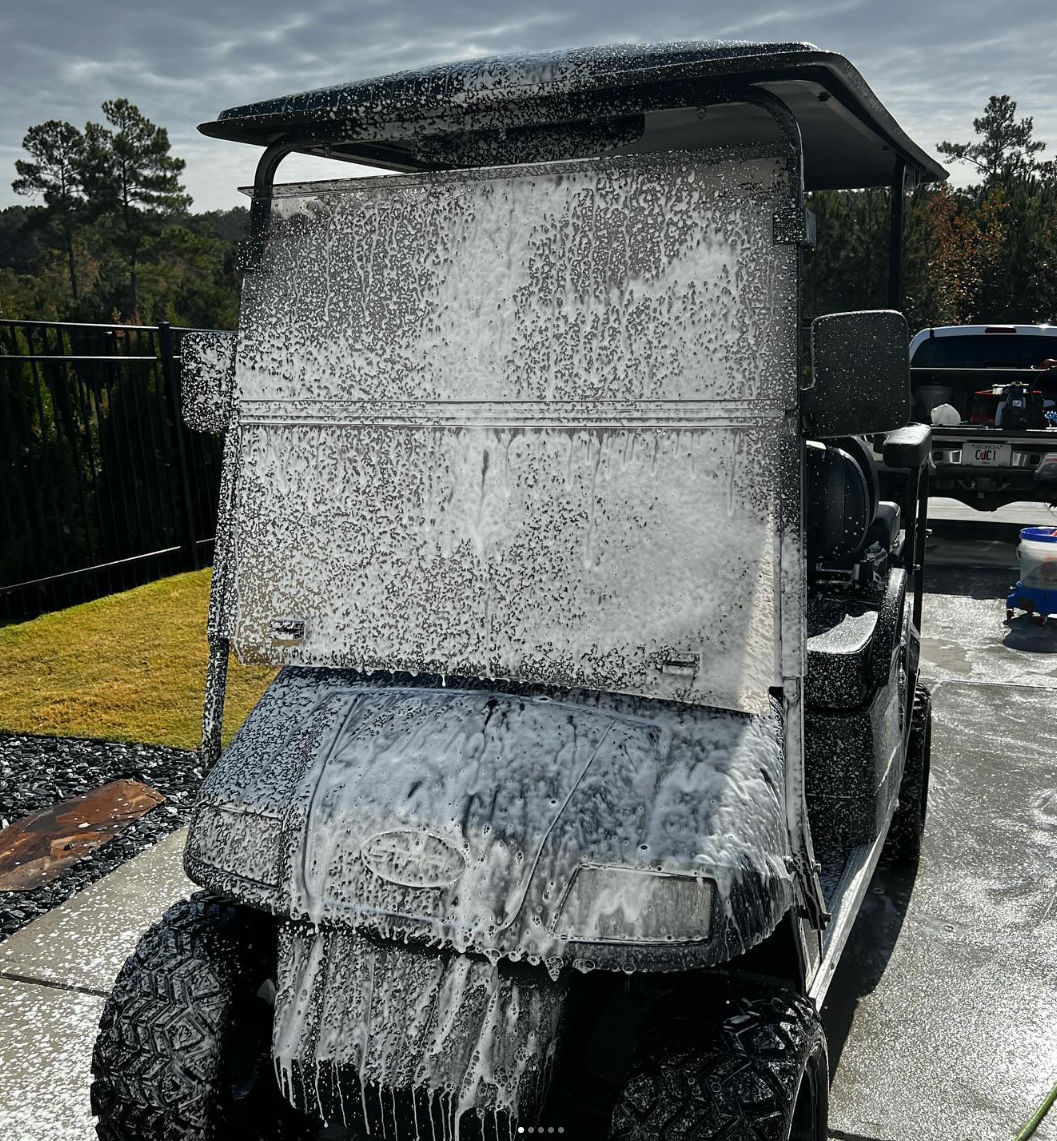 A white golf cart is parked on the grass on a golf course.