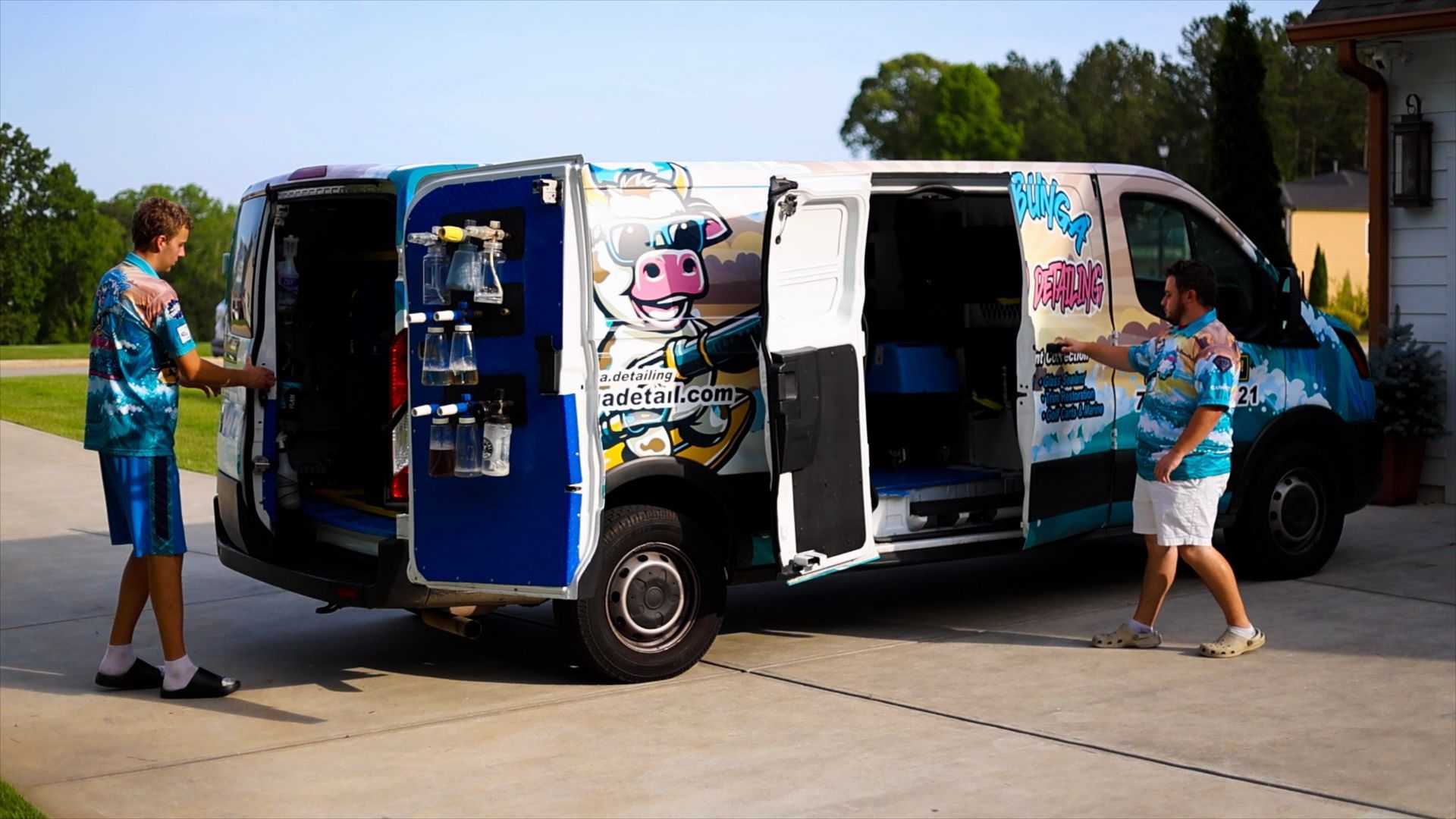 A man is washing a black car with foam in a garage.