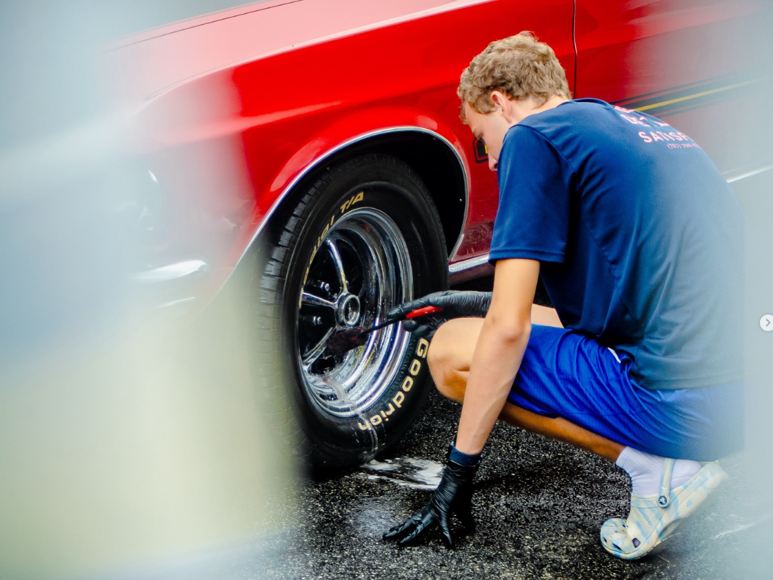 A man is kneeling down to change a tire on a red car.