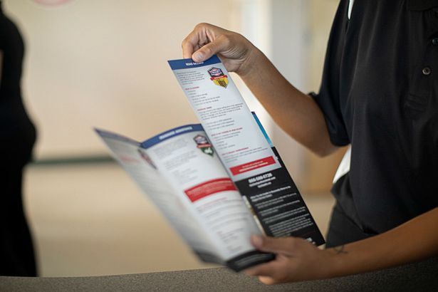 Person holding and reading a brochure with a red and blue design, possibly for an event or information.