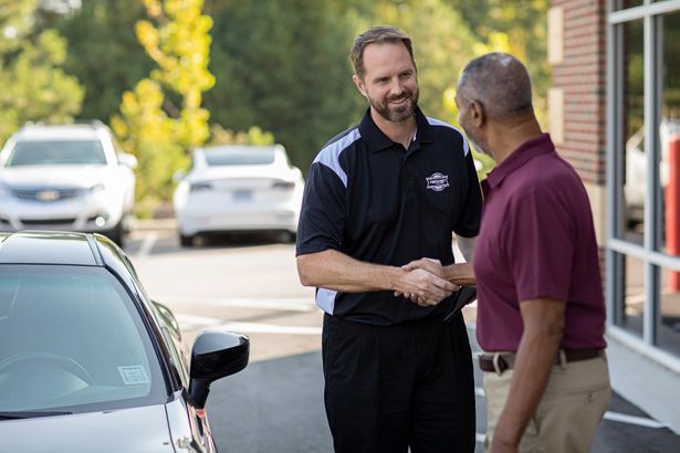 Man in uniform shakes hands with another man near a car in a parking lot.