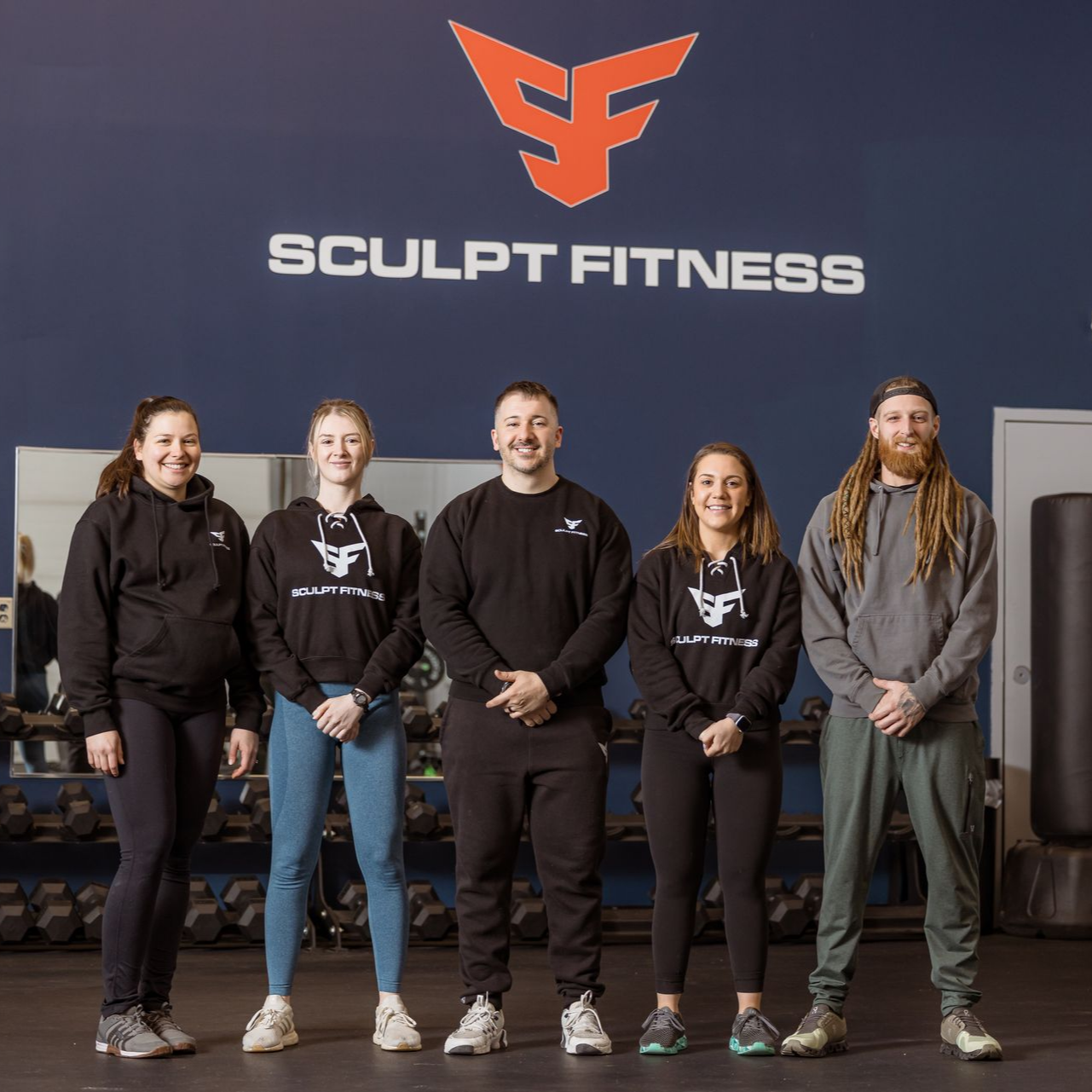Three women in workout clothes stand in a gym.