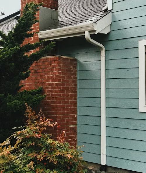 A blue house with a white gutter and a brick chimney
