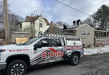 A truck is parked in front of a house with two men working on the roof.