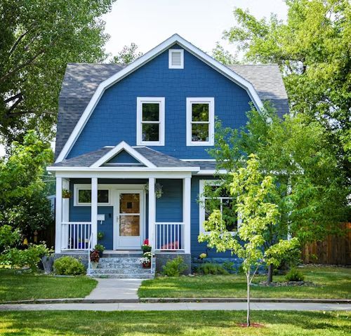 Blue house with white trim, porch, and green lawn; sunny day.