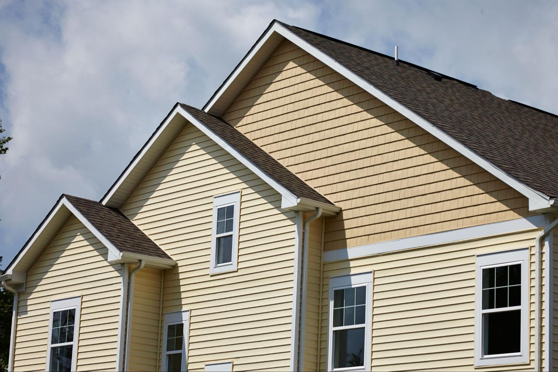 A yellow house with a brown roof and white trim