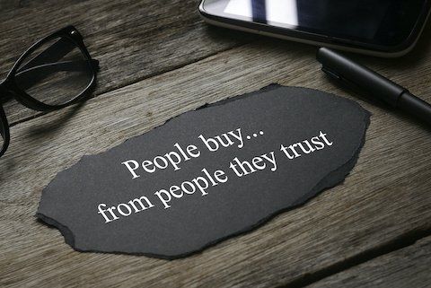 Glasses,mobile phone,pen,a a piece of black paper written with People buy...from people they trust on wooden background.