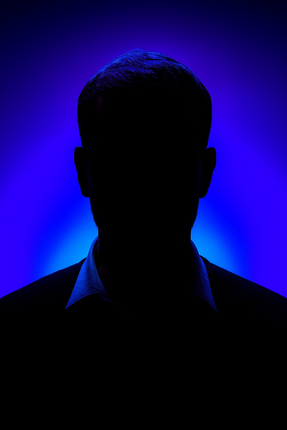 Man with dark hair and mustache in a black patterned shirt against a blue background.