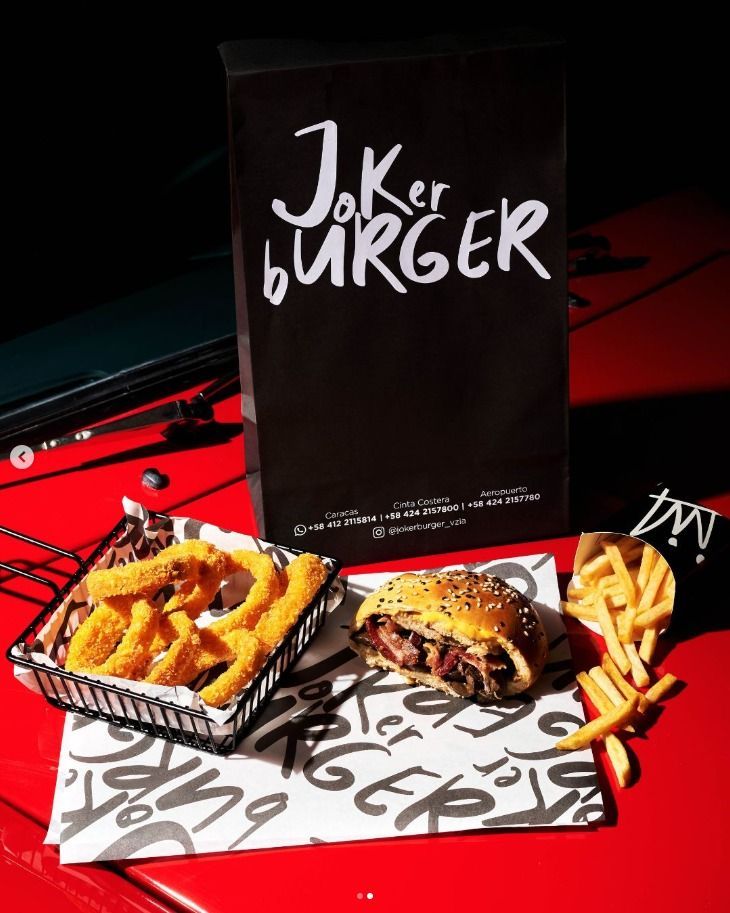 Burger, onion rings, and fries on a red table with a "Joker Burger" bag.
