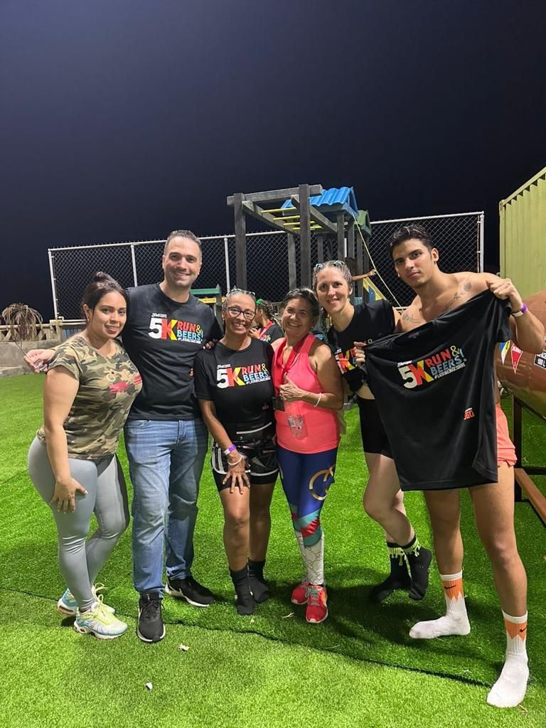 Group poses after a 5K race, smiling, holding shirts, on artificial turf at night.