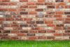 Brick wall with varied red, brown, and cream bricks, resting above a band of green grass.
