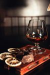 A snifter of amber liquid with dried citrus and chocolate on a wooden surface.