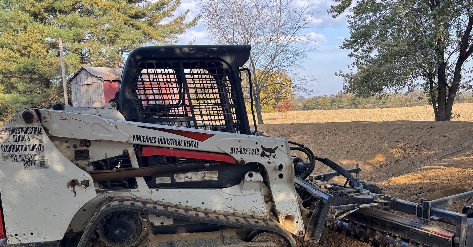 White Bobcat skid-steer tractor with a black cage, in a field, with a tree and building in the background.
