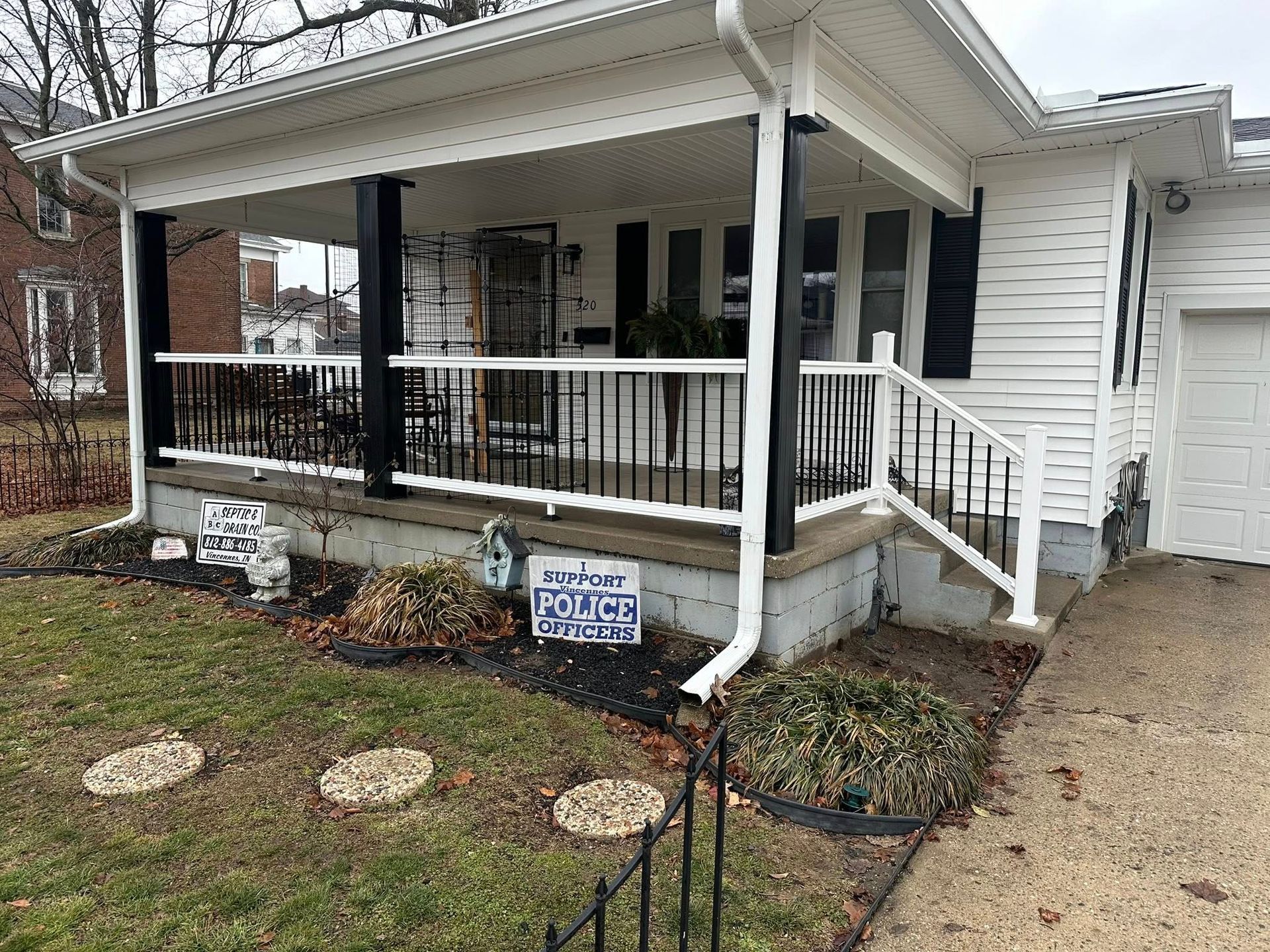 White house with black porch posts and railing, concrete steps, and small front yard garden.