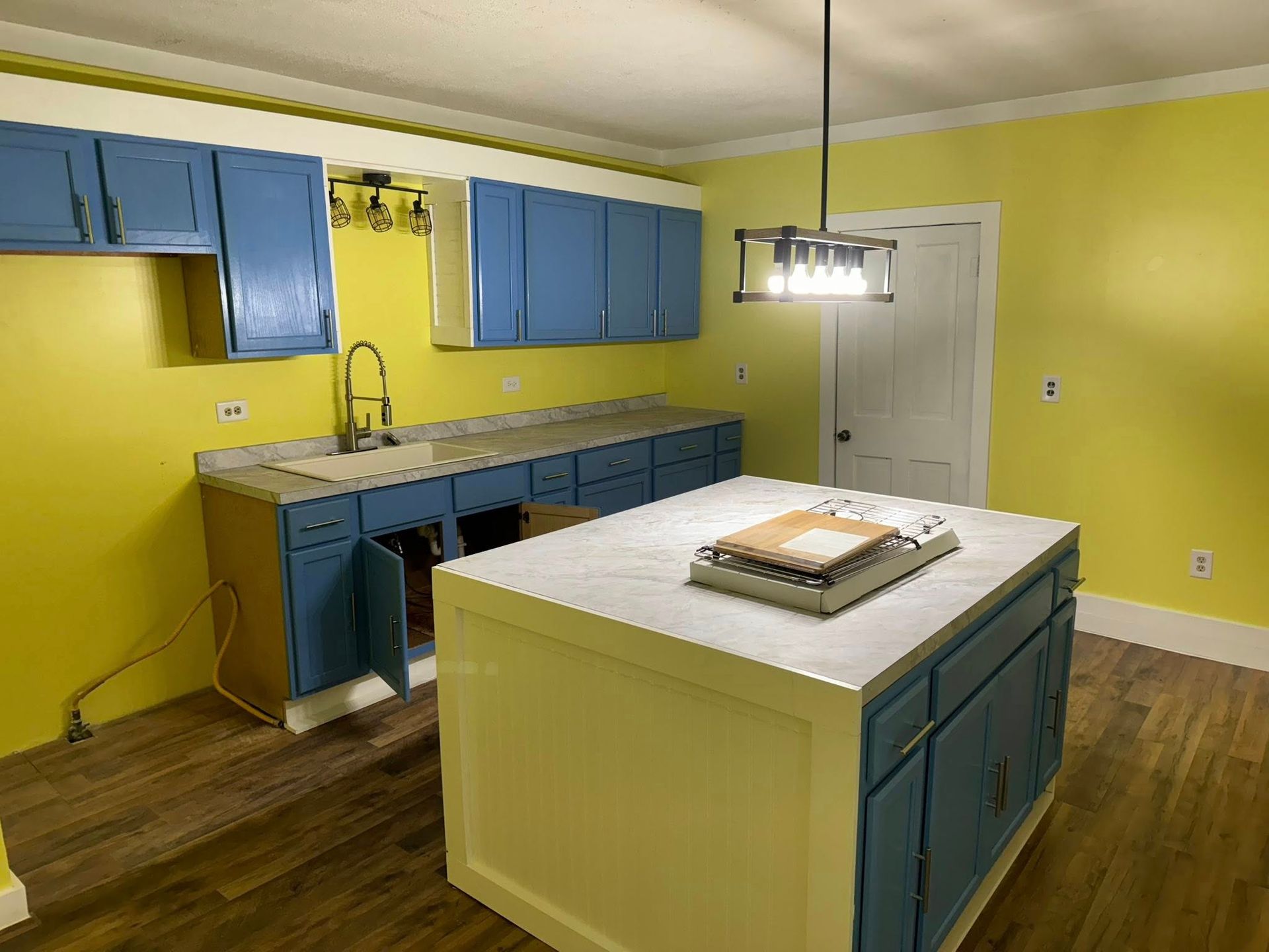 Blue cabinets and island in a kitchen with yellow walls. A faucet and light fixture are visible.
