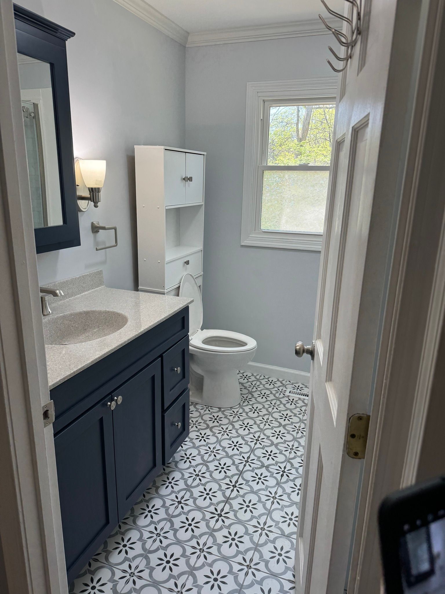 Bathroom with blue vanity, patterned tile floor, and white toilet.