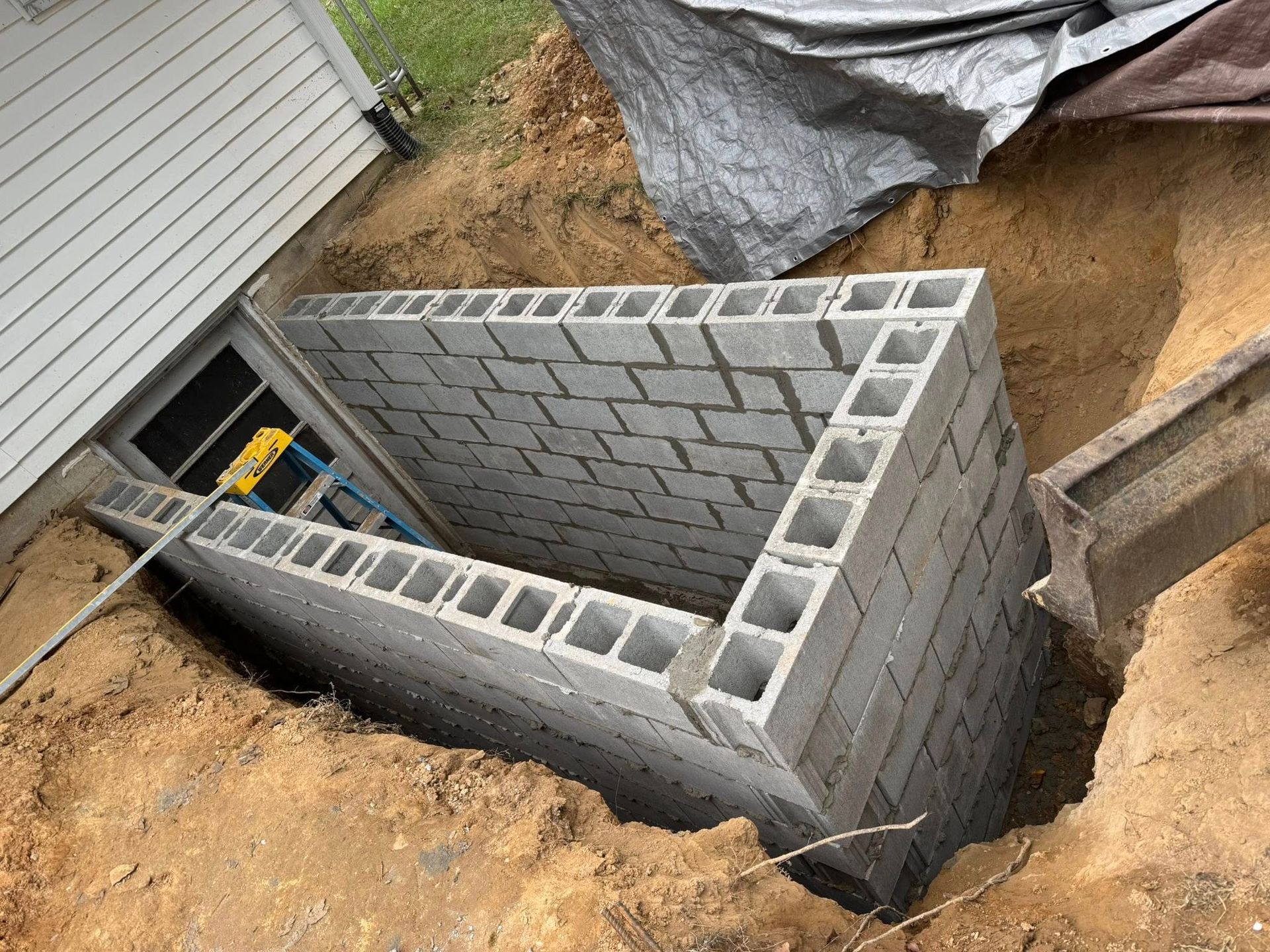 Concrete block window well under construction next to a house.