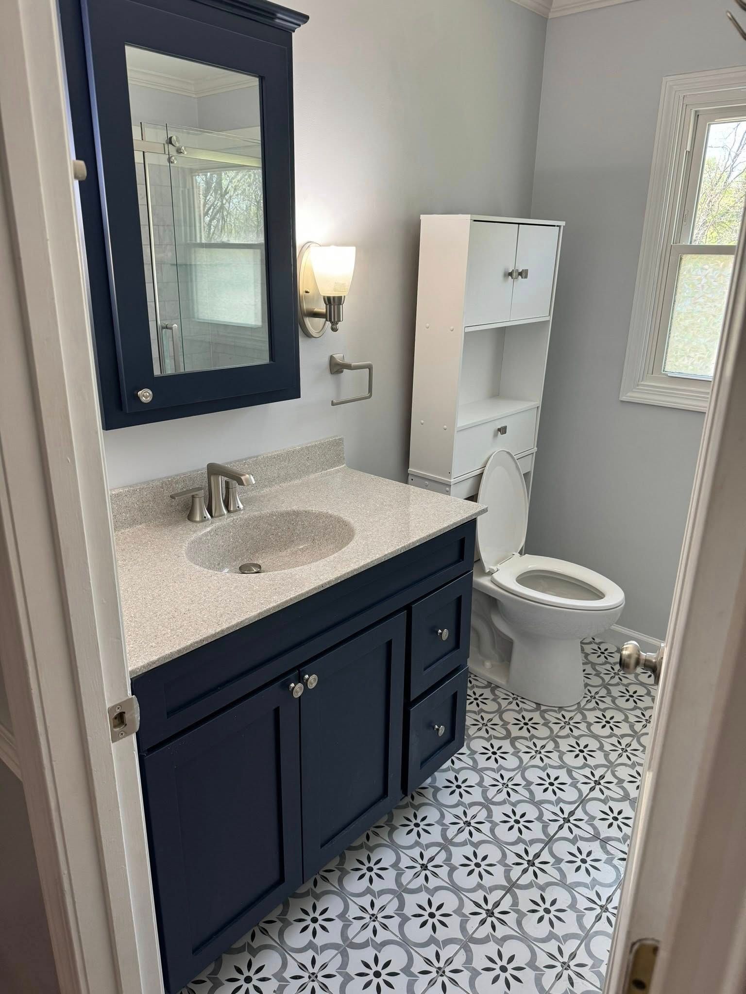 Navy blue bathroom vanity with granite countertop and patterned tile floor.