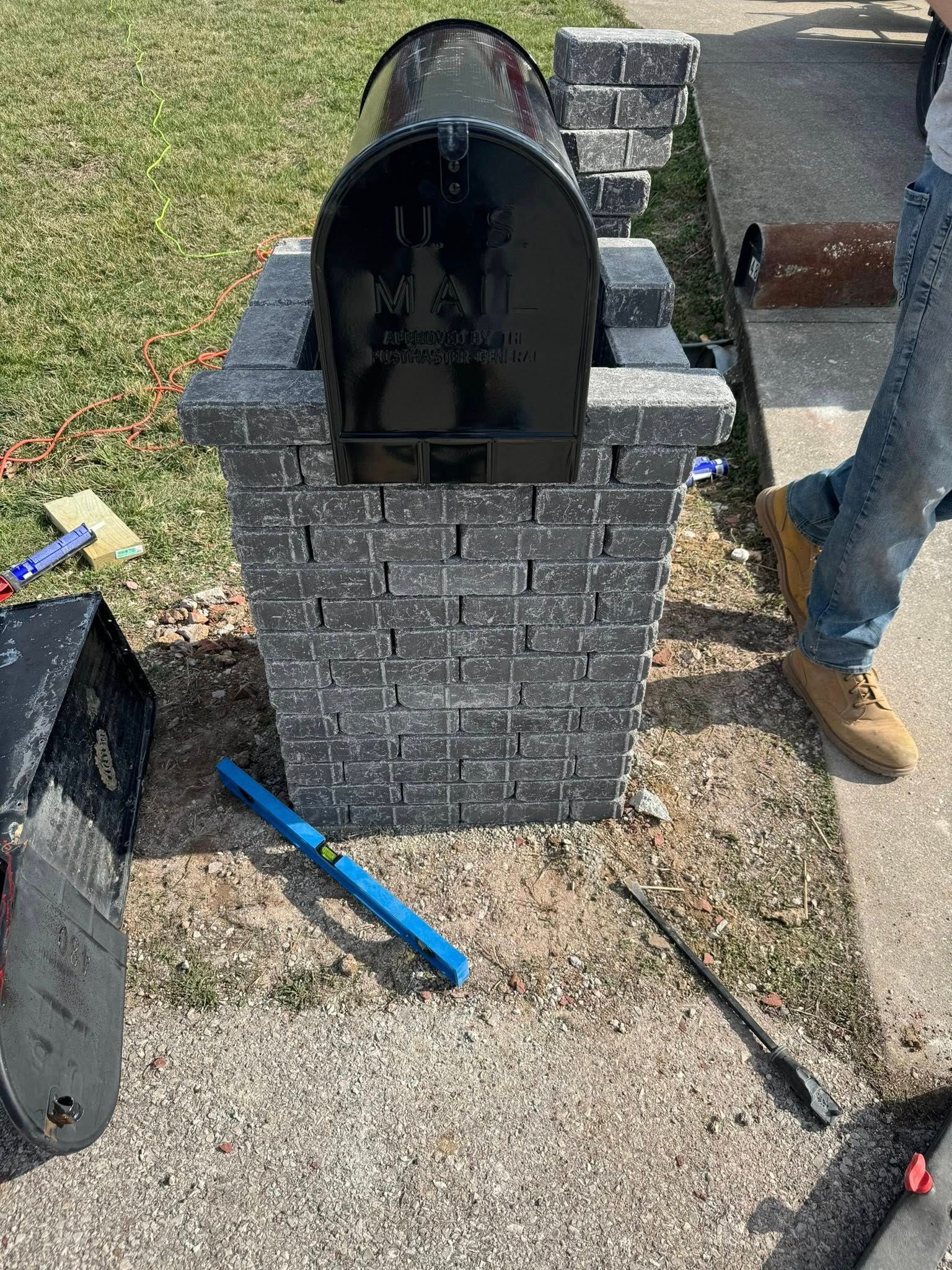 Mailbox built with brick-like blocks; person in jeans standing next to it.