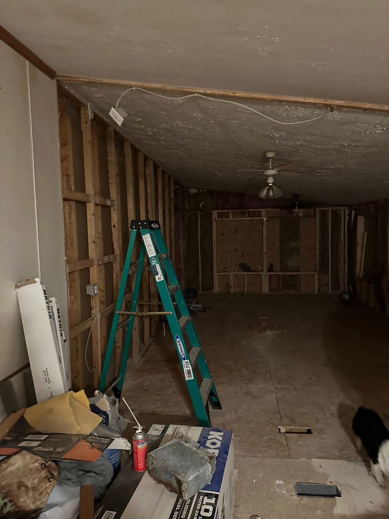 Interior room under construction with exposed wooden studs, ladder, and debris.
