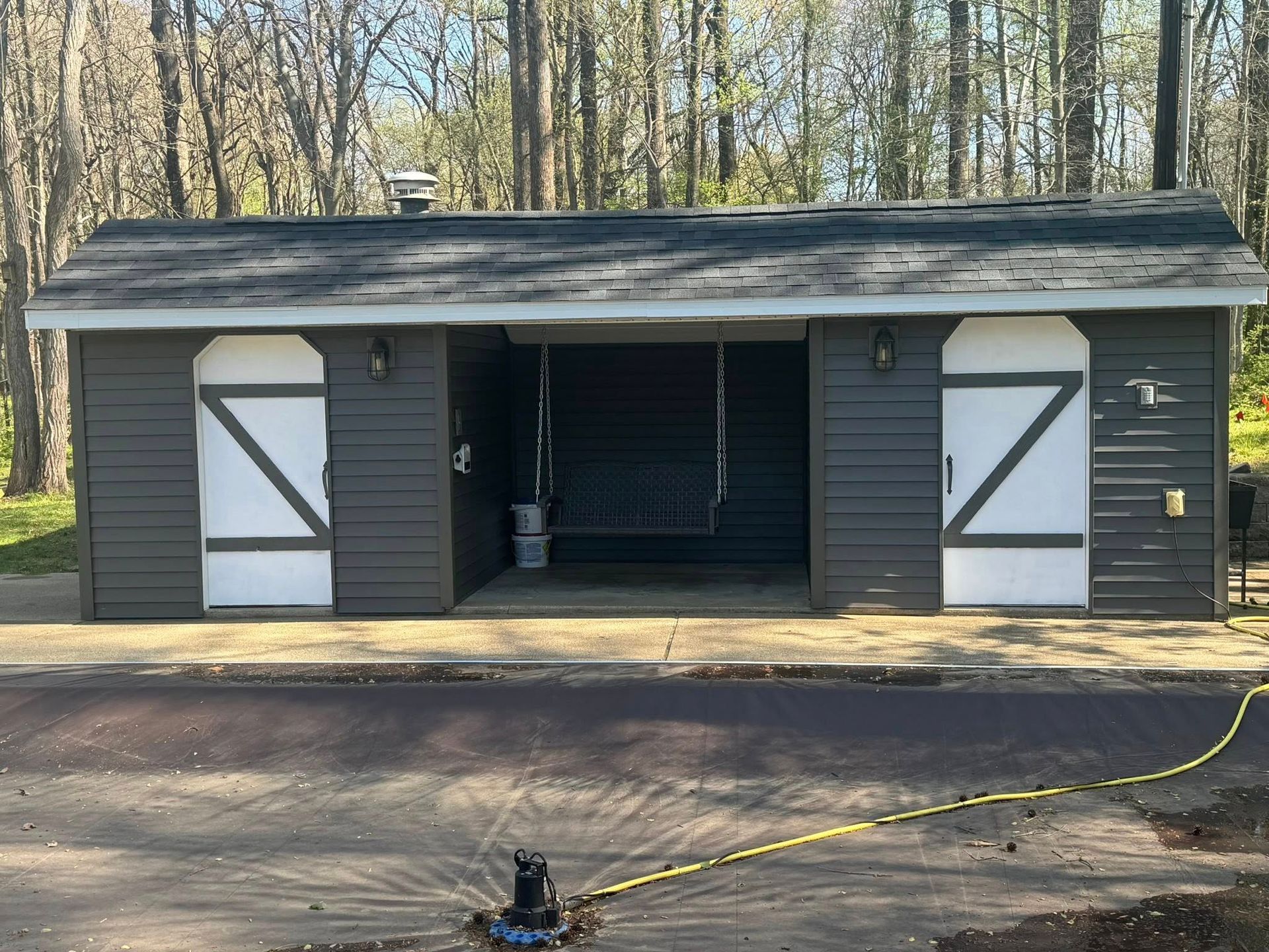 Dark gray shed with white doors, swing, and sprinkler.