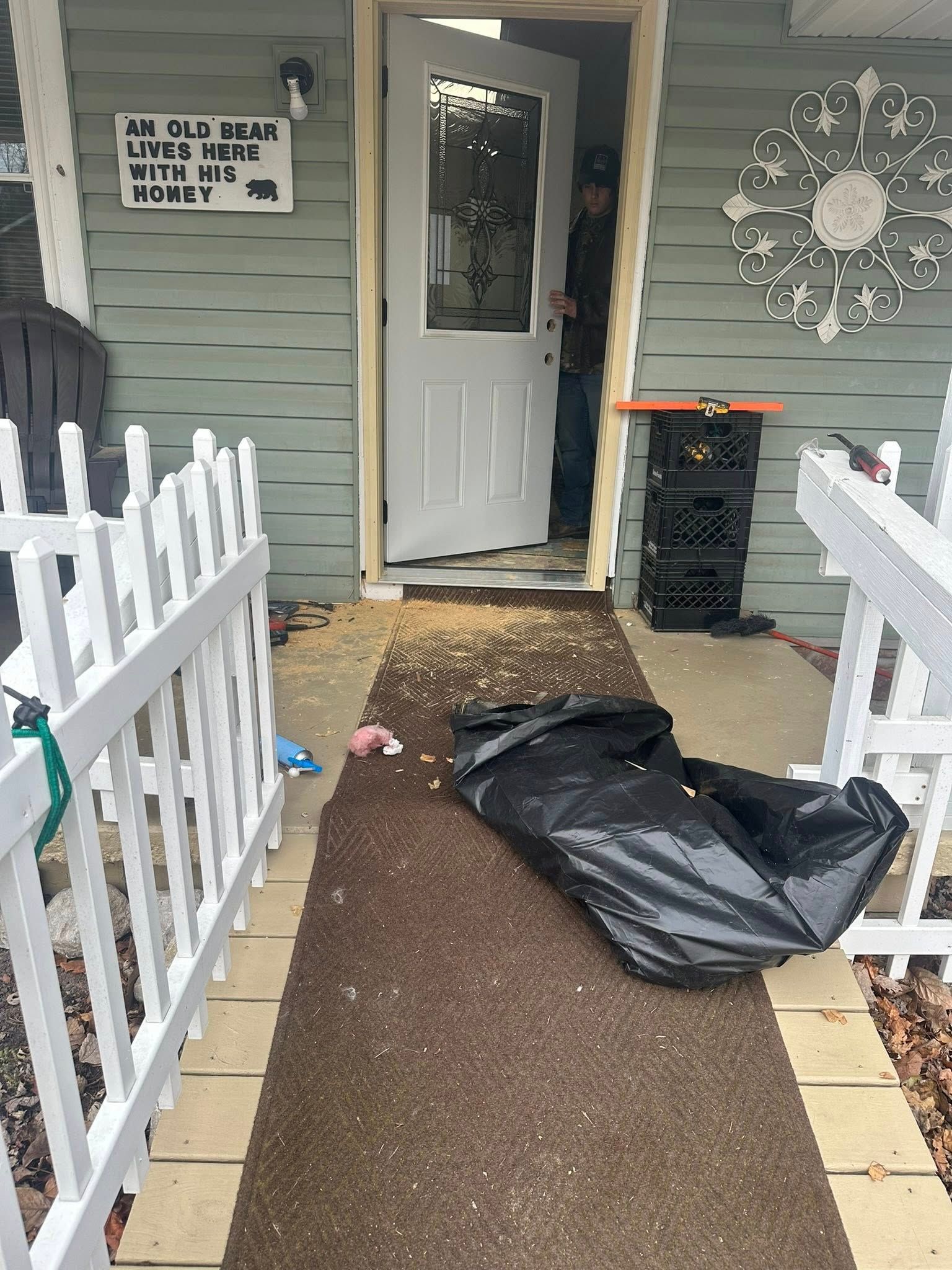 A person in doorway, trash bag on a porch, and a white fence with a sign above the door.