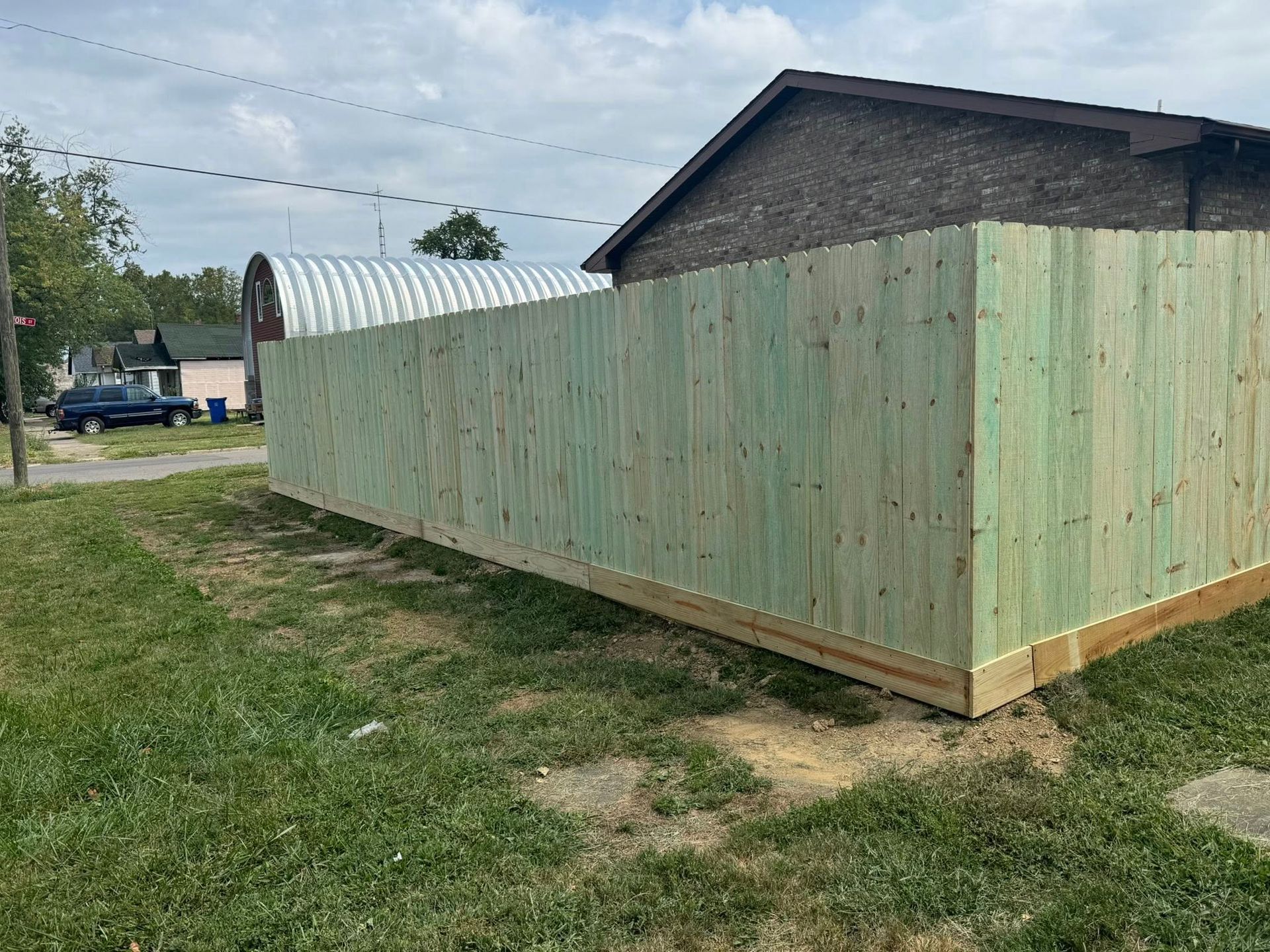 Wooden fence surrounds a yard, next to a building and grass.