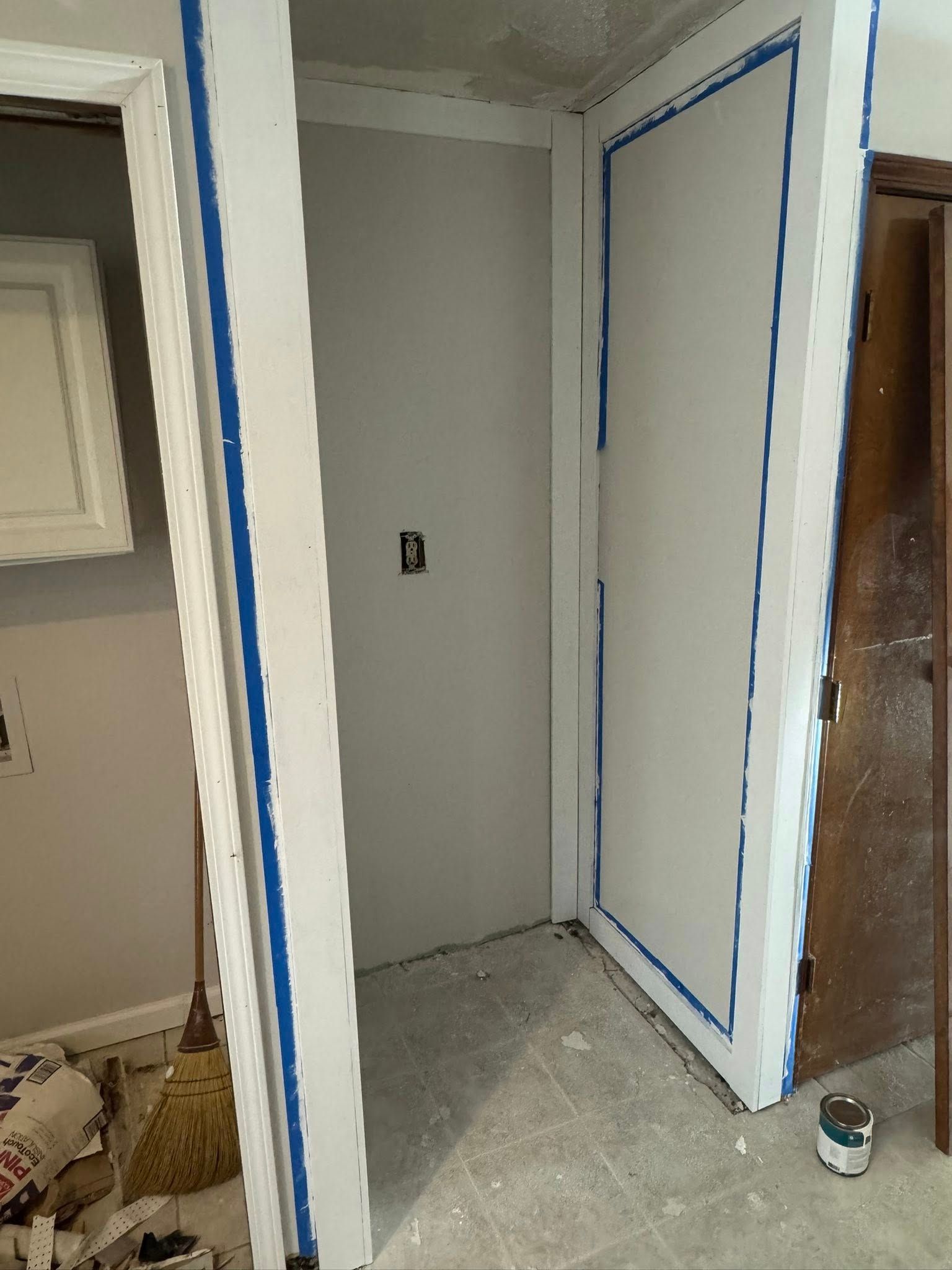 White doorway being painted with blue tape, interior wall also being painted.
