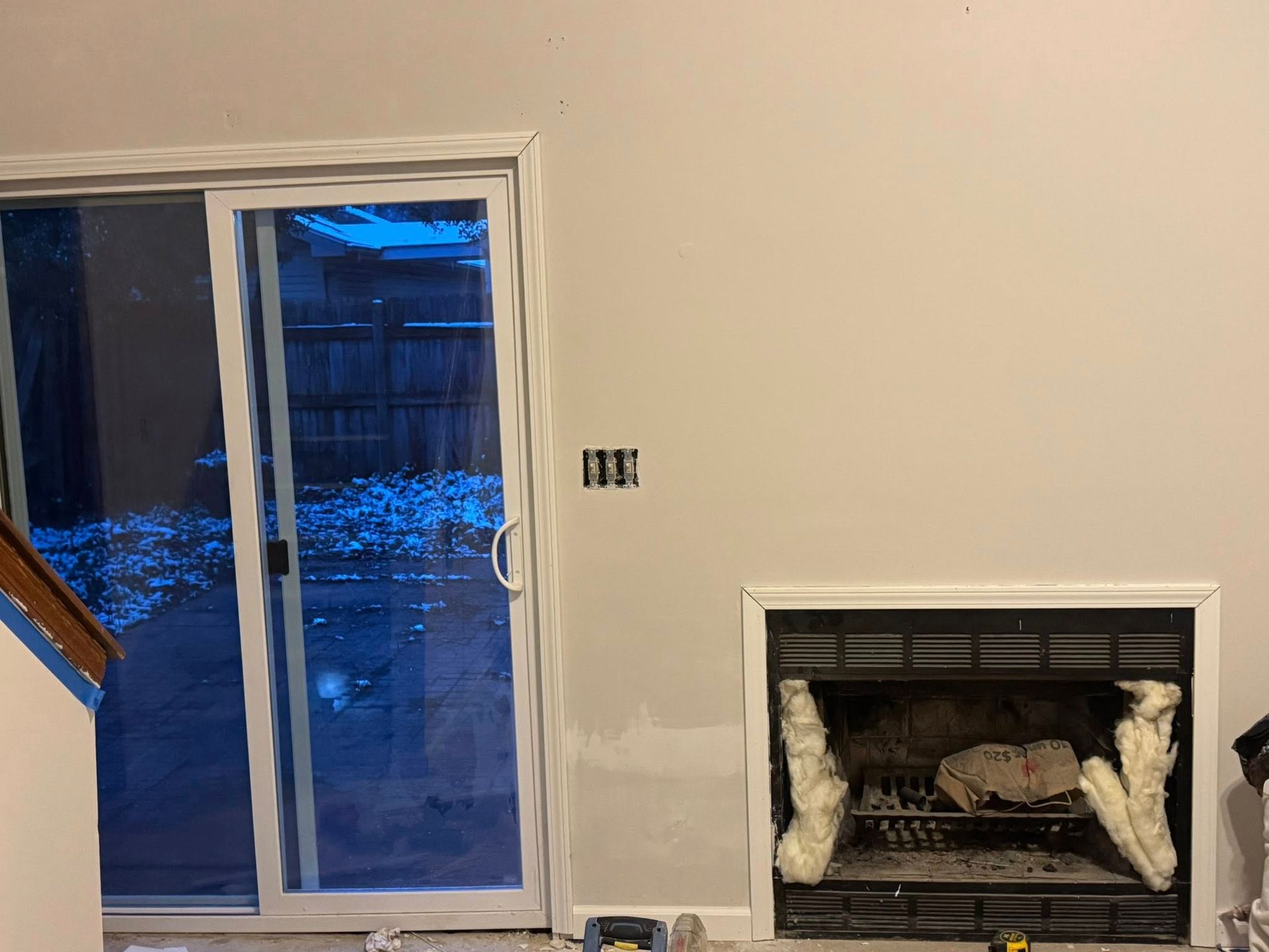 Interior wall with sliding glass door and fireplace being remodeled. Gray wall, white trim.