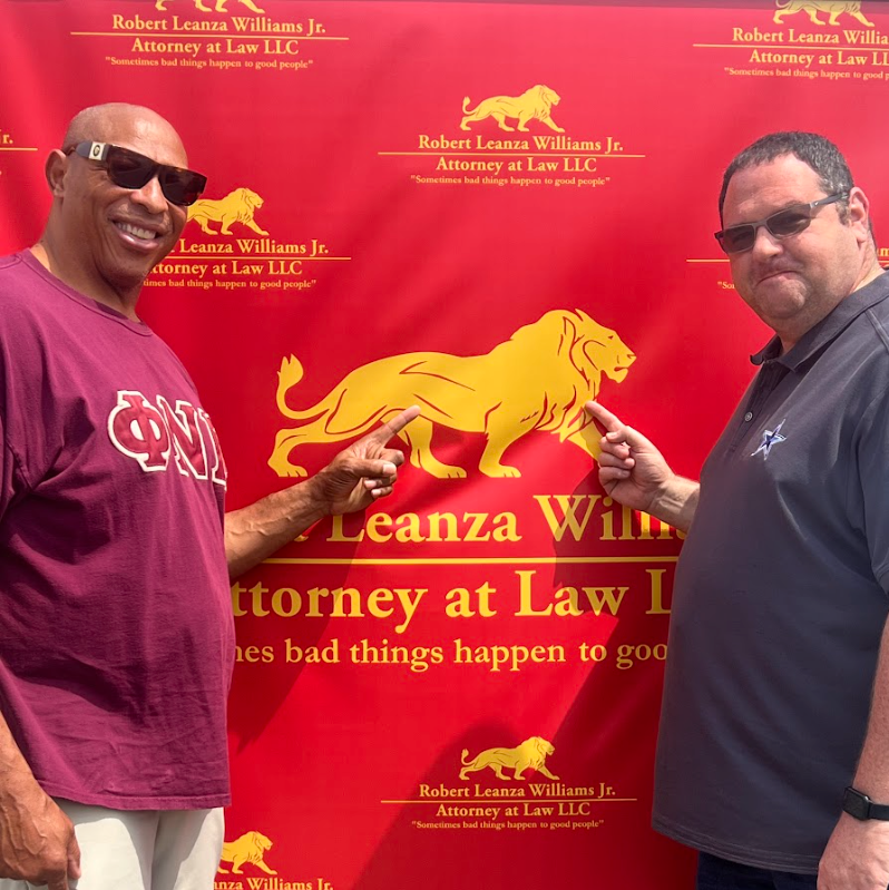 Attorney Robert Leanza Williams Jr. and a client in front of firm's step and repeat