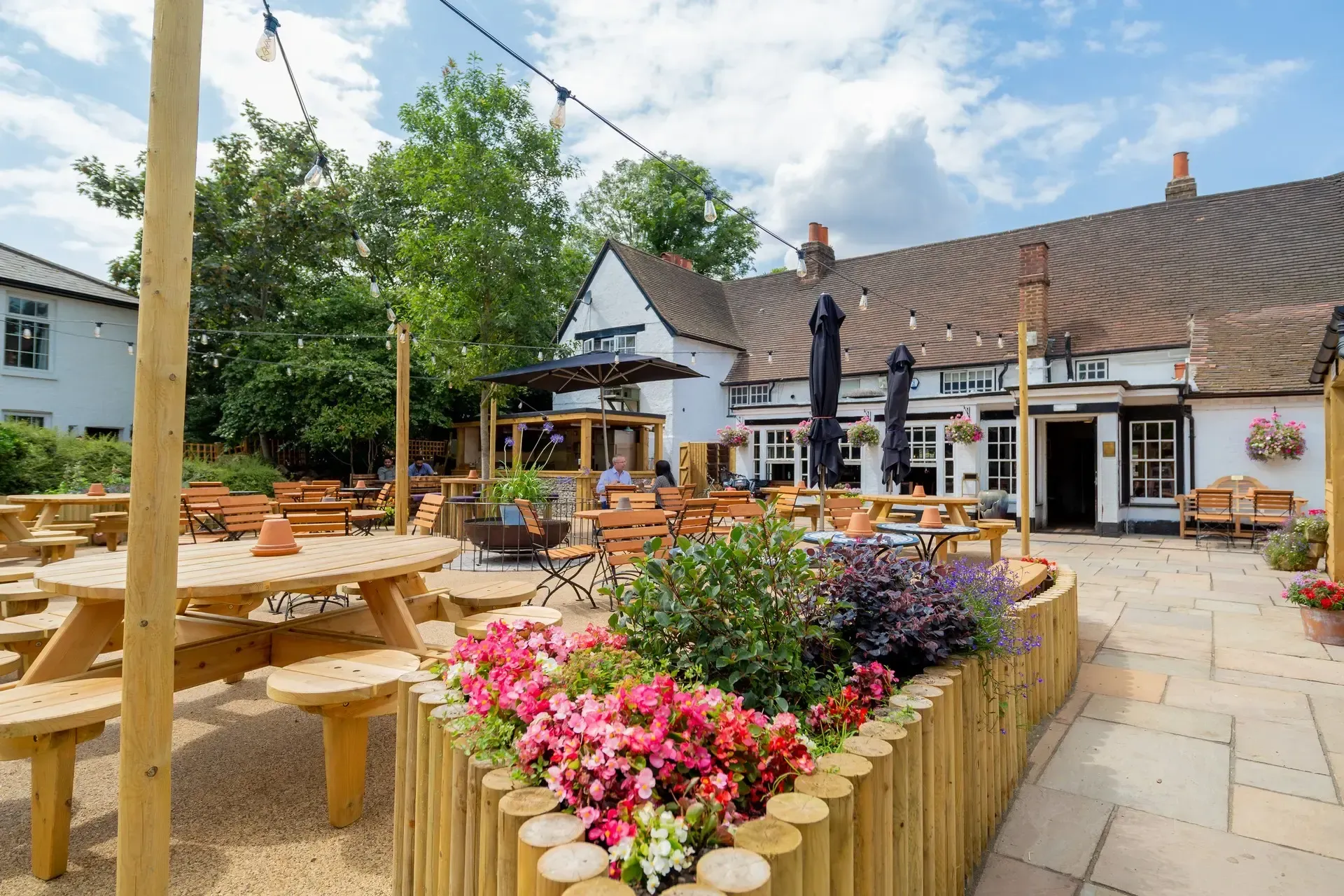 Flower-lined outdoor caf&eacute; patio with picnic tables and a rustic building under a blue sky