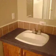 A bathroom vanity with a white drop-in sink, dark grey countertop, oak cabinets, and a framed mirror above.