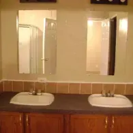 A bathroom vanity with two white sinks, wooden cabinets, and two mirrors mounted on a wall with brown tiled backsplash.