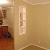 An interior view of a room with beige walls and a rectangular, white-framed window insert between two adjoining spaces.