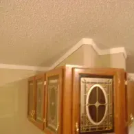 Wooden kitchen cabinets with glass inserts featuring an oval design, positioned below a white ceiling with crown molding.