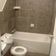 A bathroom featuring a white bathtub and toilet, with brown tiled walls and a white soap dish.