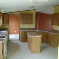 A kitchen with wood cabinets, yellow and terracotta walls, an island, and a doorway leading to another room.