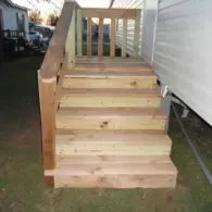 A set of newly constructed wooden outdoor steps leading up to the side entrance of a residential building.